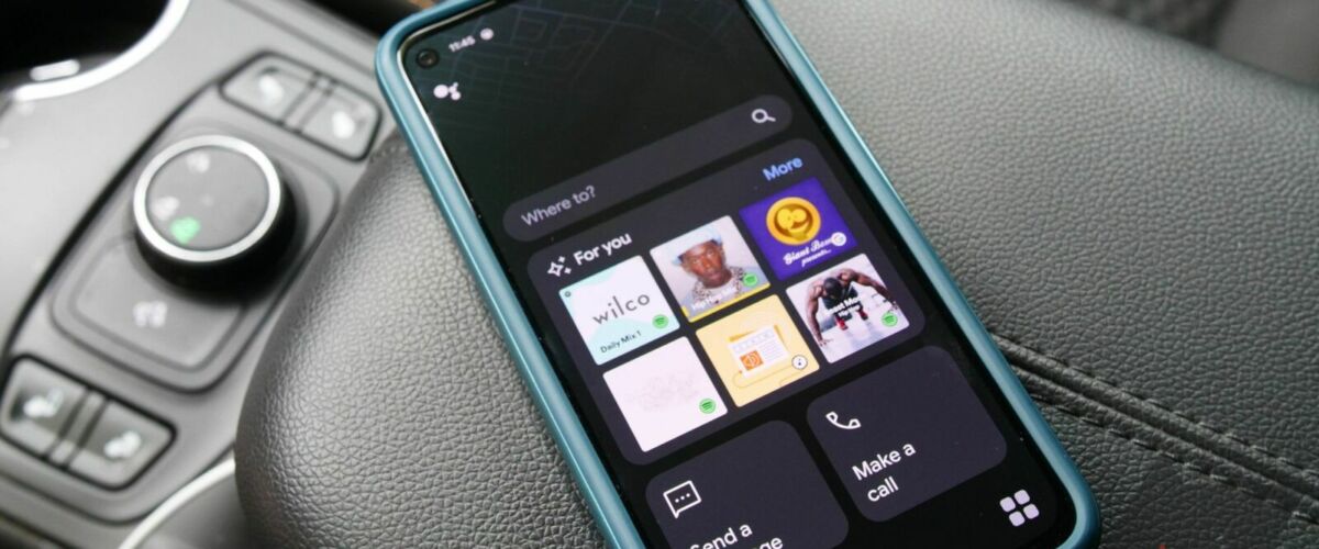 A phone running Assistant driving mode sitting on the center console of a car.