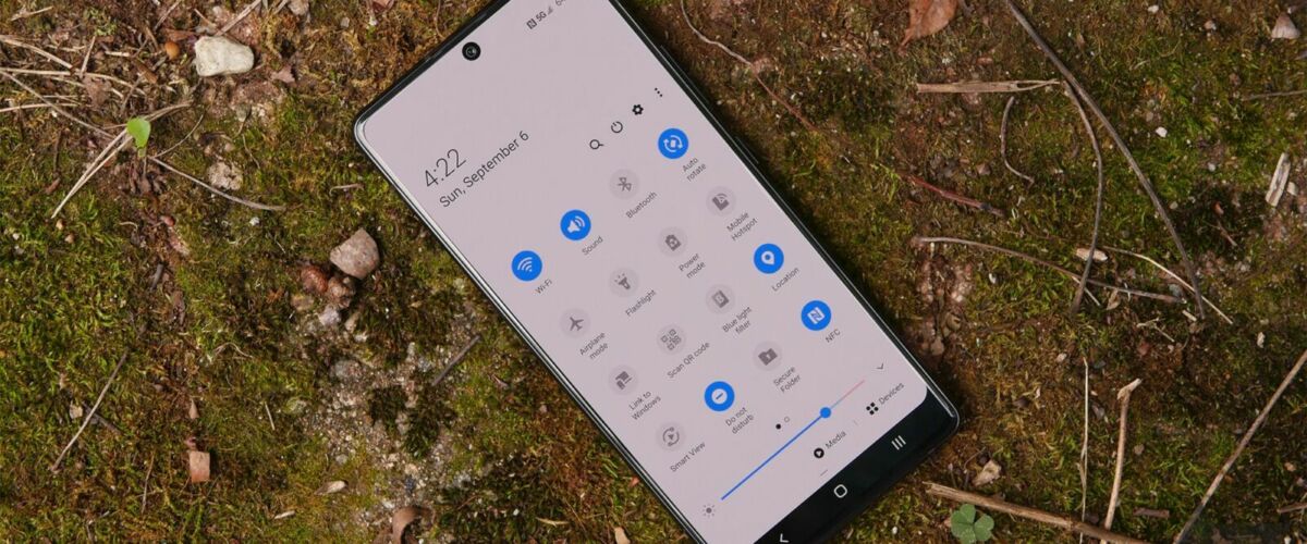 A Samsung Galaxy A71 rests on a mossy stone. The Quick Settings pulldown appears on the display.