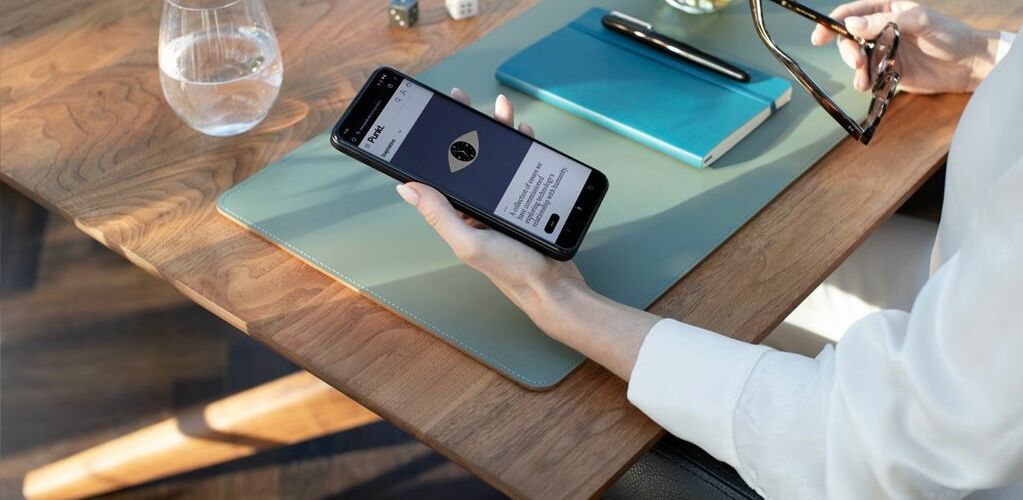 A person wearing a white shirt holds a phone while sitting at a desk.