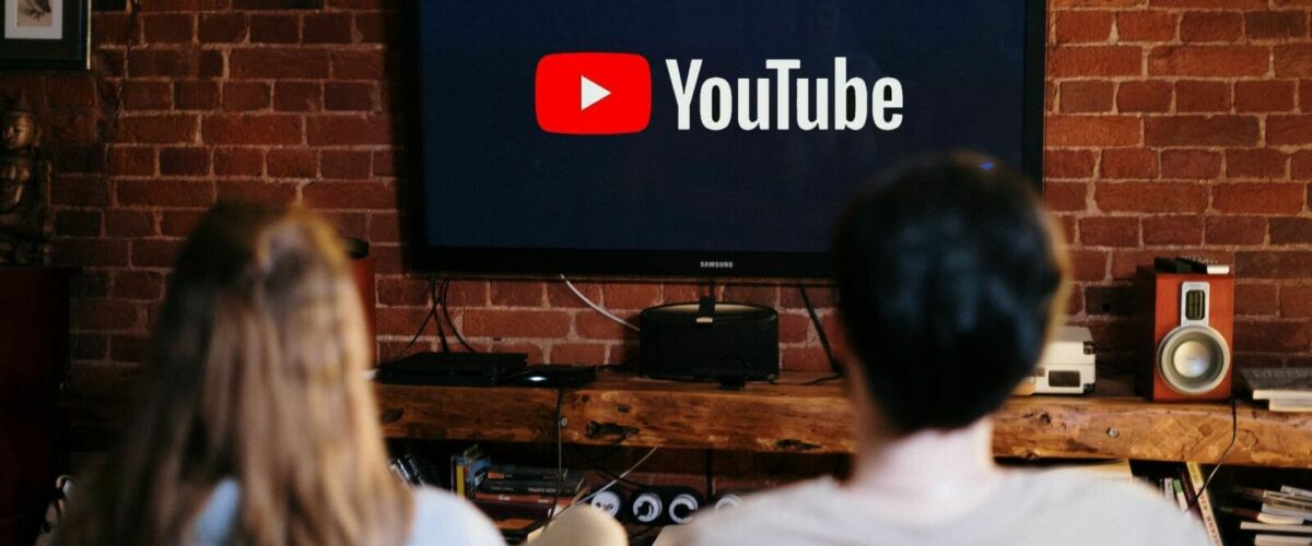 Two people are looking at a television with the YouTube logo displayed.