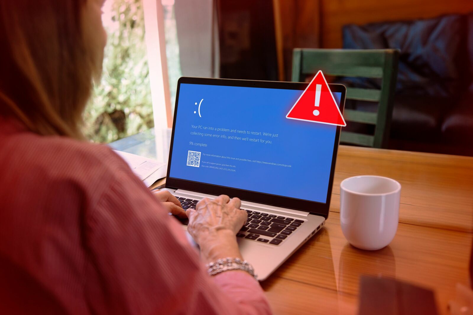 A woman using a laptop with a blue screen that appears when windows randomly shut down and an alert symbol on the front of the laptop