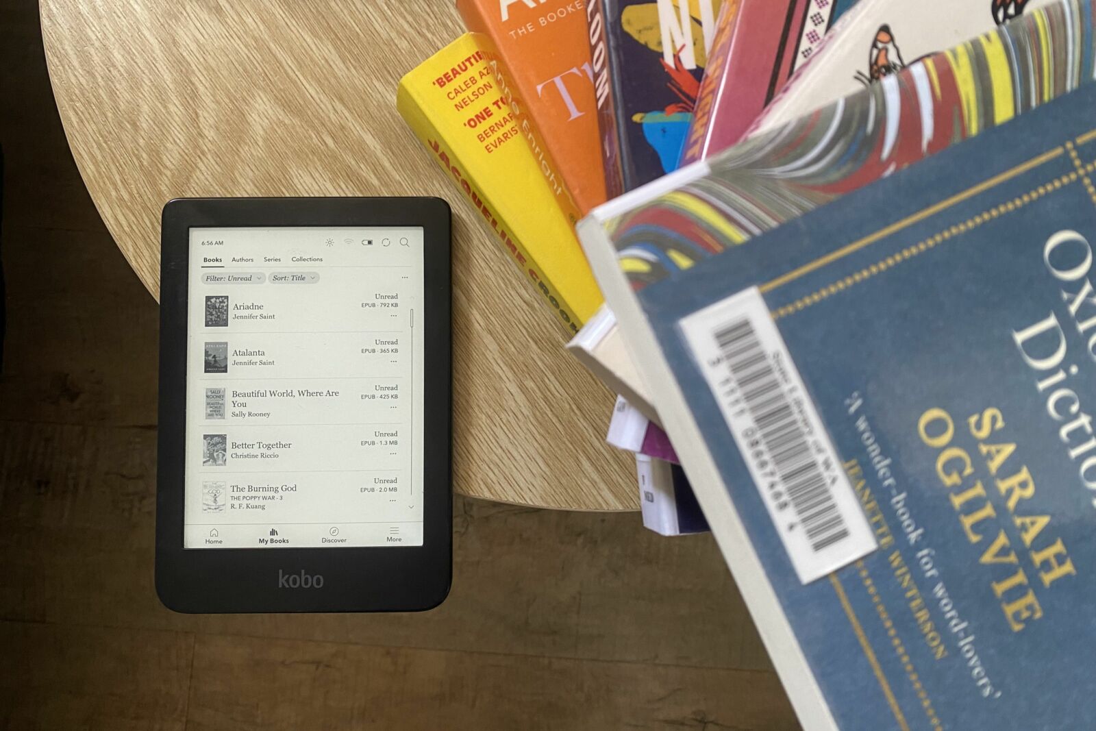 A Kobo Clara 2E eReader sitting next to a stack of books.