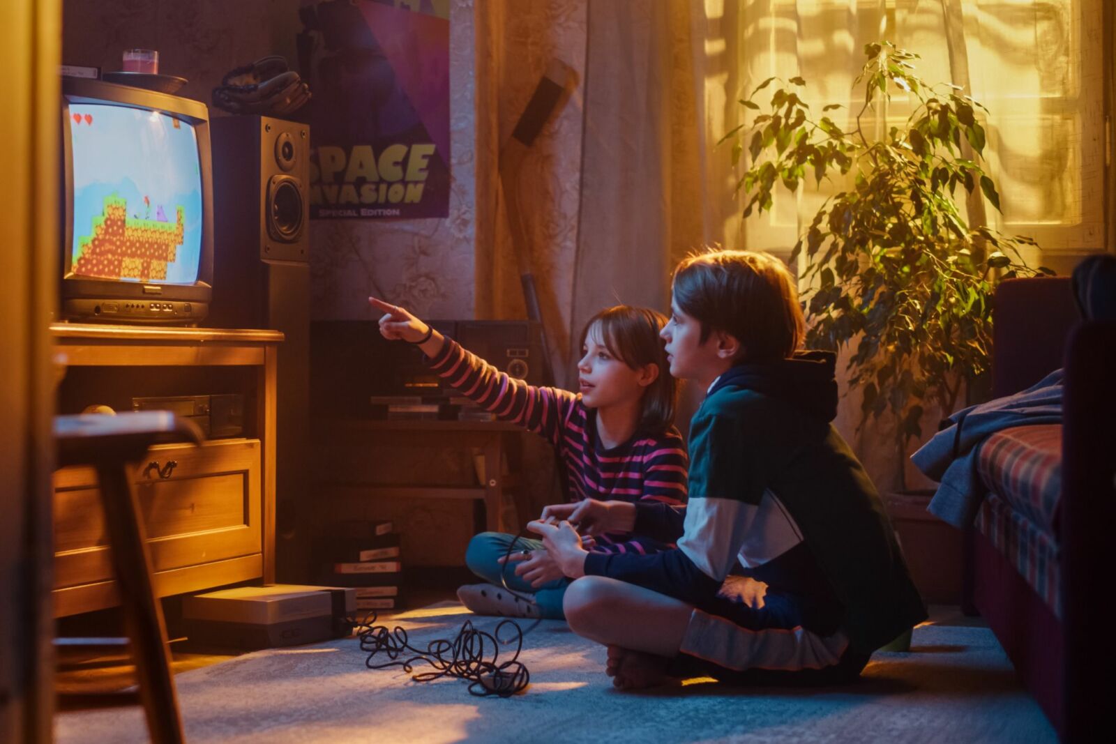 Young brother and sister playing old-school video game on a retro TV set at home.